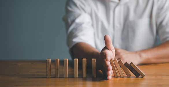 Man's hand stopping wooden blocks from falling on wooden people